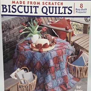 May include: A book cover titled "MADE FROM SCRATCH BISCUIT QUILTS" with a red and blue quilt on a table. The image includes a straw hat with a red ribbon, a vase of tulips, and a wooden chair.