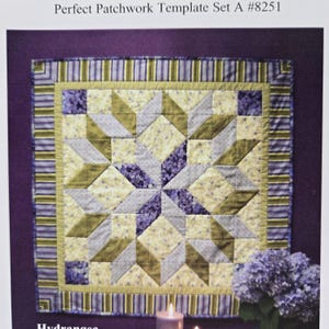 May include: A square patchwork quilt with a starburst design in shades of yellow, green, and purple. The quilt is framed by a striped border in green and purple, and the text "Perfect Patchwork Template Set A #8251" is at the top.