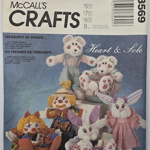 Può includere: Modello McCall's Crafts con disegni di bambole di stoffa. L'immagine mostra bambole di stoffa, tra cui orsi, un clown e conigli. Il modello include istruzioni per un cestino di stoffa e bambole.
