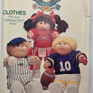 May include: Vintage Cabbage Patch Kids clothing pattern showing three dolls in sports outfits. One doll is in a baseball uniform, another in a cheerleader outfit, and the third in a football jersey with the number 10. The pattern is from Butterick.