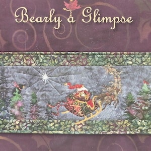 May include: A rectangular fabric wall hanging featuring the text Bearly a Glimpse at the top. The central scene depicts a Santa Claus figure in a sleigh pulled by reindeer flying over a forest of pine trees under a bright star, framed by a green leaf border.