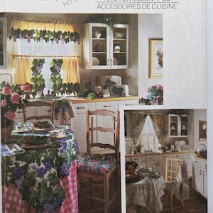 May include: A vintage kitchen design with a table set for a meal, a chair with a floral cushion, and grape-themed curtains. White cabinets and a framed picture add to the classic kitchen aesthetic. The image is from a Simplicity House pattern.