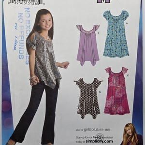 Puede incluir: Un patrón de costura para niñas de tallas grandes 8 1/2-16 1/2, con varios diseños de vestidos. La imagen incluye a una joven que lleva un top plateado con lentejuelas y pantalones oscuros. El patrón es de Simplicity.