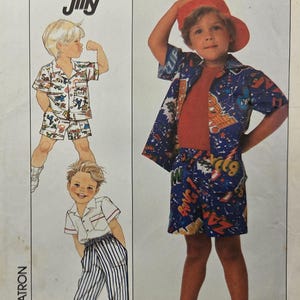 Può includere: Modello di cucito Simplicity per abbigliamento per bambini. Il modello presenta illustrazioni di ragazzi che indossano vari outfit, tra cui un completo camicia a maniche corte e pantaloncini con una stampa grafica a fumetti e un completo pantaloni e camicia a righe.