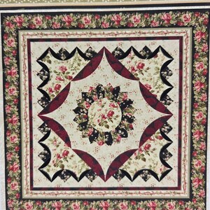 May include: A floral quilt with a cream background and a central circular design. The quilt features red roses, black accents, and a decorative border with more roses. The quilt's dimensions are not visible in the image.