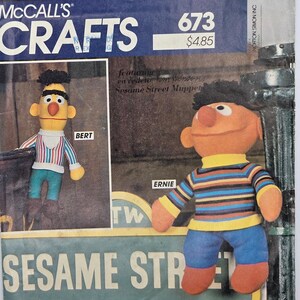 Peut inclure: Une pochette de patron de couture McCall's Crafts 673 représentant Bert et Ernie de Sesame Street. La couverture montre une poupée jaune Bert avec un haut rayé et un pantalon bleu, et une poupée orange Ernie avec un pull à rayures et un pantalon bleu.