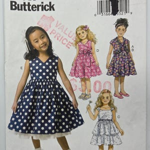 May include: A Butterick B6046 sewing pattern for children's dresses. The pattern shows illustrations of girls in different dress styles, including a blue polka dot dress, a pink floral dress, and a white dress. Sizes available: 2-3-4-5.