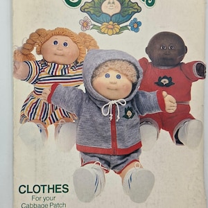 May include: Vintage Cabbage Patch Kids clothing pattern. The pattern features three dolls wearing different outfits. One doll is in a striped dress, another in a gray tracksuit, and the third in a red outfit. The pattern is from Butterick.