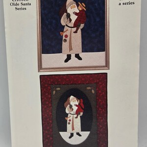 May include: A paper pattern titled SANTA & CHILD, 10th in a series, featuring two illustrations of Santa Claus holding a child. The top image shows a framed Santa in a light coat, while the bottom image shows an oval-framed Santa in a red coat.