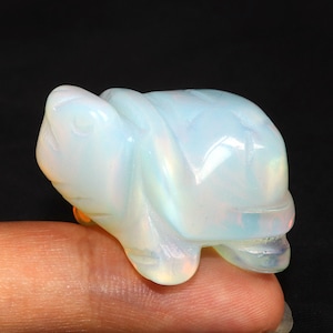 Puede incluir: Una pequeña figurita de tortuga de ópalo blanco. La tortuga está tallada en ópalo blanco translúcido con colores arcoíris iridiscentes.