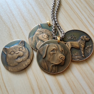 May include: Four bronze-colored pet pendant necklaces. Each pendant features a different pet: a cat, a dog with its tongue out, a dog, and a dog with the word "Lucky". The pendants are attached to a silver chain.