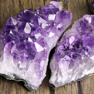 Könnte beinhalten: Zwei große Amethyst-Kristallgruppen mit einem Farbverlauf von Lila zu Weiß. Die Kristalle sind in einer natürlichen Formation mit scharfen Spitzen und einer rauen Textur angeordnet.