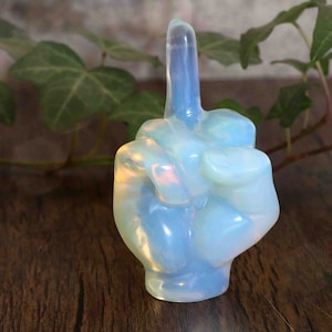 Könnte beinhalten: Eine Handskulptur aus irisierendem Opal, mit dem Mittelfinger ausgestreckt in einer unhöflichen Geste. Die Skulptur ist hellblau mit einer weißen Basis.