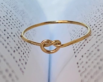 May include: A gold knot ring on a white book.
