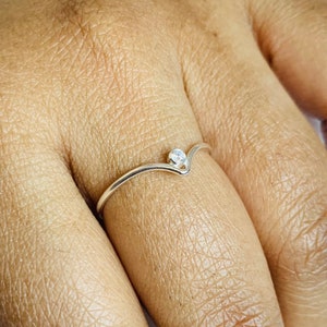 May include: A delicate gold ring with a single, clear gemstone set in a V-shaped band.
