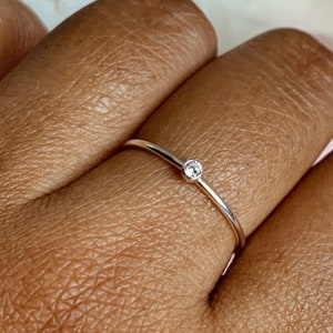 May include: A delicate silver ring with a single, small, clear gemstone set in the centre.