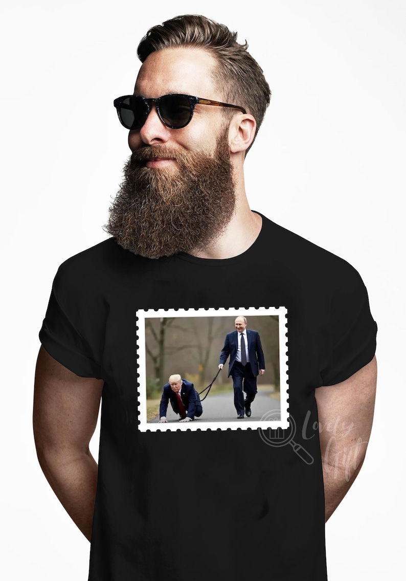 May include: A black t-shirt with a white border around a picture of two men. The man in the front is on his hands and knees, while the man behind him is walking and holding a leash attached to the man in front. The text "la" is visible in the bottom right corner of the image.
