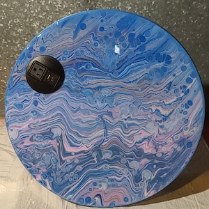 May include: A round, blue and white table top with a swirling, marbled pattern. The table top has a black electrical outlet cover in the center.