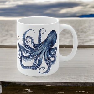 Puede incluir: Una taza de cerámica blanca con una ilustración azul y blanca de un pulpo. El pulpo tiene ocho tentáculos y está representado en un estilo realista y detallado.