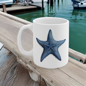 Peut inclure: Une tasse &agrave; caf&eacute; en c&eacute;ramique blanche avec une illustration d'&eacute;toile de mer bleue. L'&eacute;toile de mer a un design textur&eacute; et d&eacute;taill&eacute;.