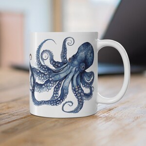 May include: A white ceramic mug with a blue and white octopus illustration. The octopus has eight tentacles and is depicted in a detailed, realistic style.