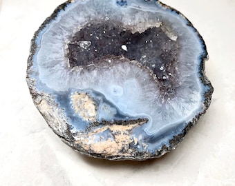 May include: A large, round, gray and blue agate geode with a hollow center lined with white crystals.