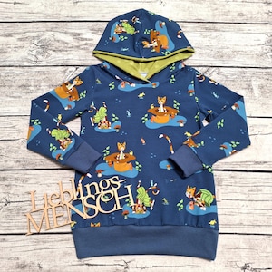 Könnte beinhalten: Ein dunkelblaues Langarm-Kapuzensweatshirt mit einem wiederkehrenden Muster aus orangefarbenen Füchsen mit Hüten und grünem Blattwerk. Die Innenseite der Kapuze ist hellgrün. Ein Holzschild mit dem Text LIEBLINGS MENSCH liegt auf der linken Seite.