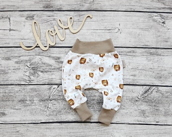 Könnte beinhalten: Weiße Babyhose mit braunem Bärenmuster und braunem elastischem Bund. Die Hose hat einen umgeschlagenen Beinabschluss.