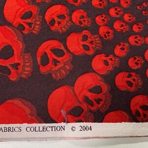 Op de afbeelding: Stof met rood schedelpatroon met de tekst "Fabrics Collection &copy; 2004" op een wit label.