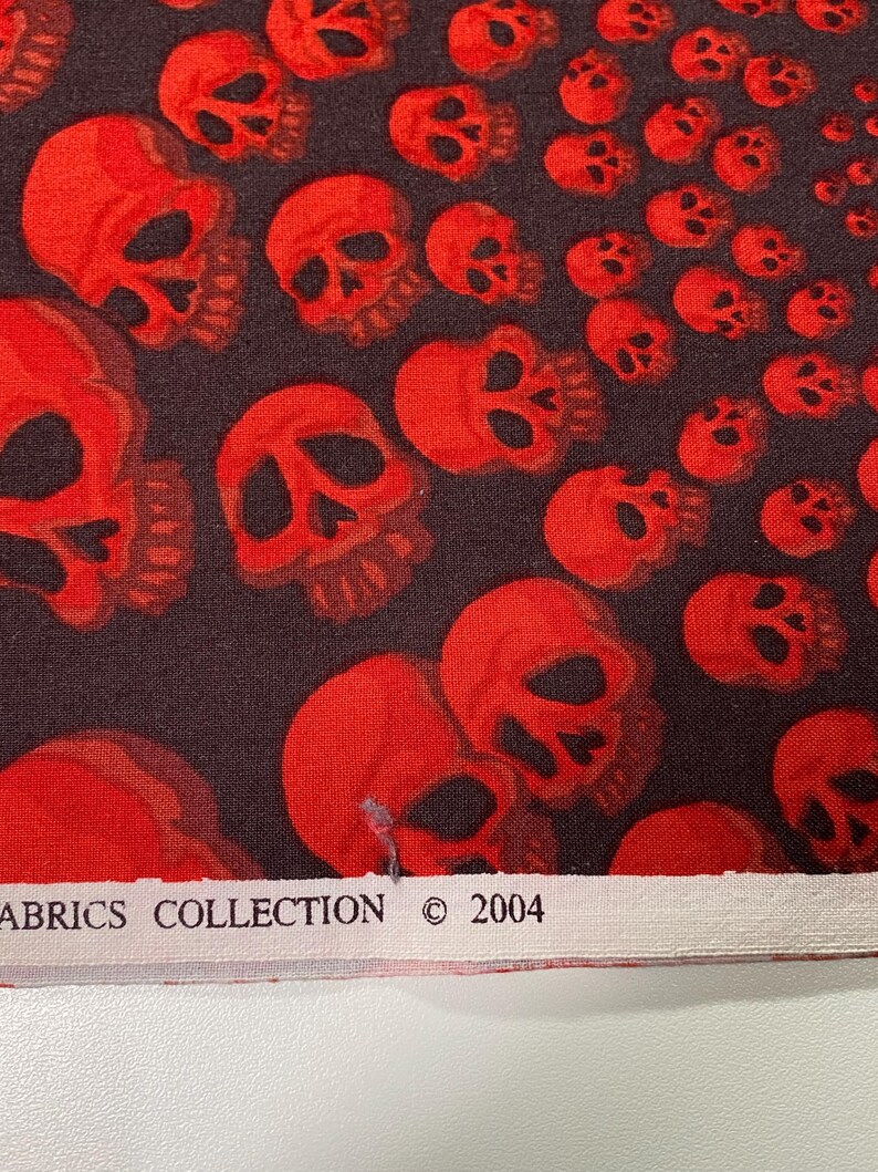 Op de afbeelding: Stof met rood schedelpatroon met de tekst "Fabrics Collection &copy; 2004" op een wit label.