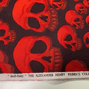Op de afbeelding: Stof met rood schedelpatroon met de tekst "skull-finity" THE ALEXANDER HENRY FABRICS COLLECTION.