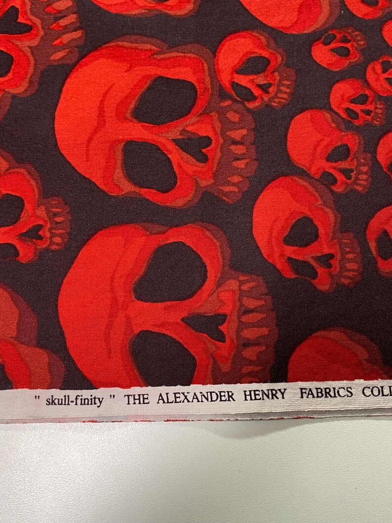 Op de afbeelding: Stof met rood schedelpatroon met de tekst "skull-finity" THE ALEXANDER HENRY FABRICS COLLECTION.