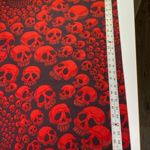 Op de afbeelding: Stof met een rood schedelpatroon met een herhalend ontwerp. De stof is zwart met rode schedels in verschillende maten.