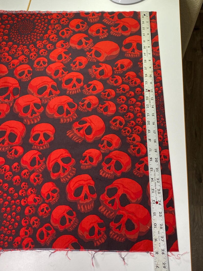Op de afbeelding: Stof met een rood schedelpatroon met een herhalend ontwerp. De stof is zwart met rode schedels in verschillende maten.
