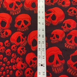 Op de afbeelding: Stof met een rood schedelpatroon en een liniaal die 66 cm meet. De stof is zwart met een herhalend patroon van rode schedels in verschillende maten.