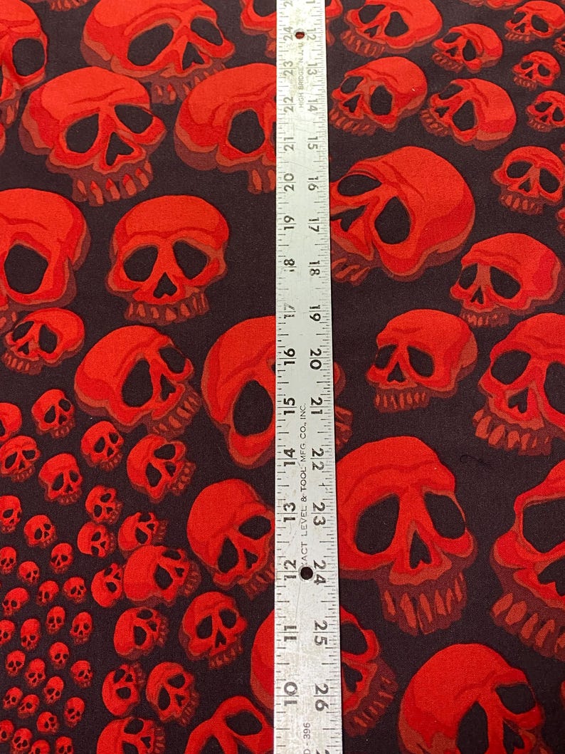 Op de afbeelding: Stof met een rood schedelpatroon en een liniaal die 66 cm meet. De stof is zwart met een herhalend patroon van rode schedels in verschillende maten.