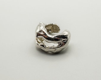 May include: A silver-colored ear cuff with an organic, textured design. The cuff has an open, flowing shape with a smooth, polished finish. The jewelry piece is designed to be worn on the ear.