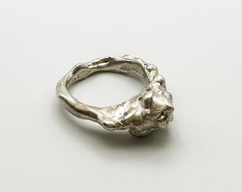 May include: A silver ring with a textured, organic design. The ring is made of metal and has a unique, abstract shape.