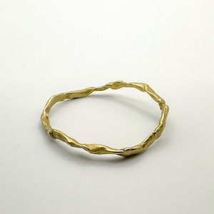 Op de afbeelding: Een gouden armband met een gedraaid, organisch ontwerp.