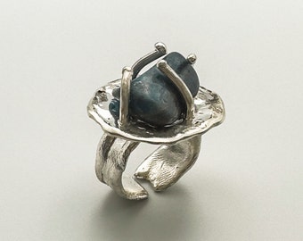 May include: A silver ring with a blue-green stone set in a textured silver band. The stone is held in place by a silver frame.