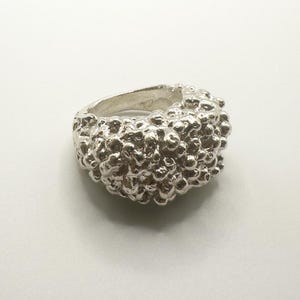 Puede incluir: Un anillo de plata con un diseño texturizado con forma de burbujas. El anillo es grueso y tiene una forma redondeada.