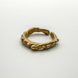 May include: A gold ring with a textured, organic design. The ring is open and appears to be made of metal.