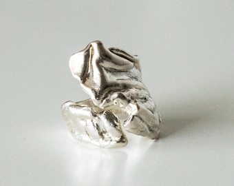 May include: A silver ring featuring an open, irregular, and organic shape with a textured, molten-like surface. The metal has a reflective finish with deep crevices and raised ridges that create a sculptural, uneven form around the band.