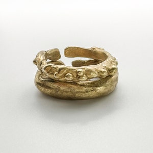 Peut inclure: Deux bagues en or, l'une avec un design texturé et organique, l'autre avec une surface lisse et arrondie. Les bagues sont empilées l'une sur l'autre.