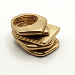 Op de afbeelding: Een stapel van vijf gouden metalen ringen. De ringen hebben allemaal verschillende vormen, sommige zijn ronder en andere zijn puntiger. De ringen zijn op elkaar gestapeld, met de grootste ring onderaan en de kleinste ring bovenaan.