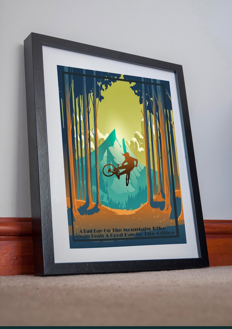 May include: A framed poster with a retro design featuring a mountain biker jumping over a mountain peak in a forest setting. The poster has the text "A Bad Day On The Mountain Bike Always Beats A Good Day In The Office".