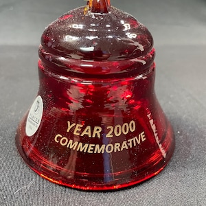 May include: A red glass bell with a gold inscription that reads "YEAR 2000 COMMEMORATIVE".