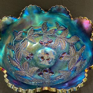 Puede incluir: Cuenco de vidrio azul iridiscente con borde ondulado y dise&ntilde;o de cerezas y hojas. El cuenco tiene un borde festoneado con ribete dorado. La superficie del cuenco refleja una gama de colores, incluyendo azul, verde y morado.