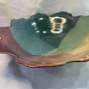 May include: A handmade ceramic bowl with a unique, organic shape. The bowl features a color gradient from brown to green to yellow. The rim has a wavy, irregular edge. The bowl is suitable for serving food or as a decorative piece.