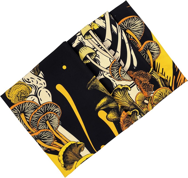 May include: Folded black fabric with a repeating pattern of yellow and orange mushrooms. The design features various mushroom types with detailed illustrations. The fabric has a yellow border and a cream-colored background.